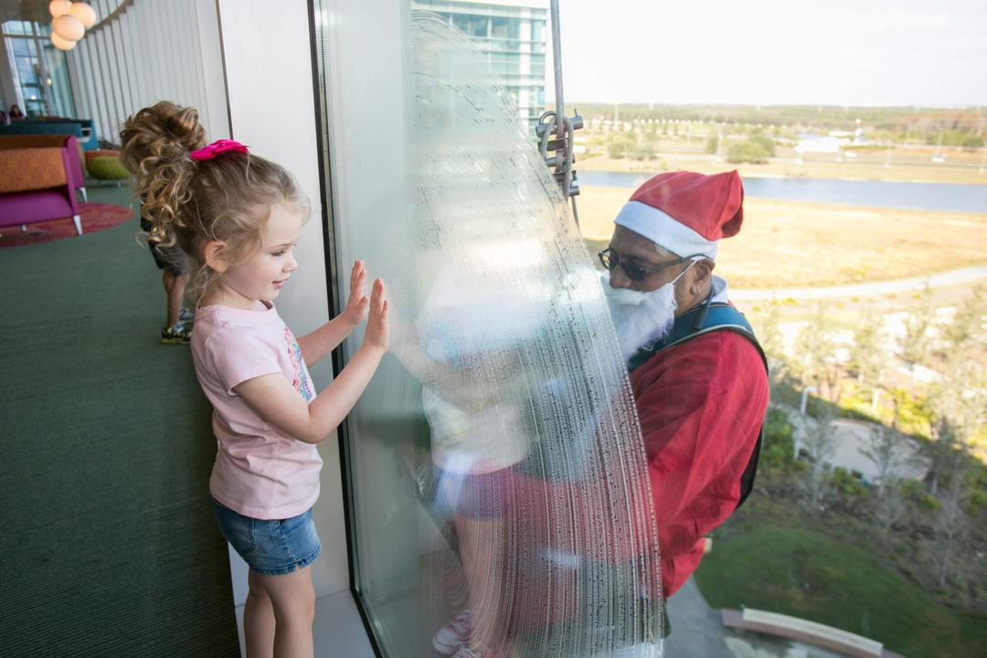 Santa washing office window with little girl on the other side of the window smiling at Santa