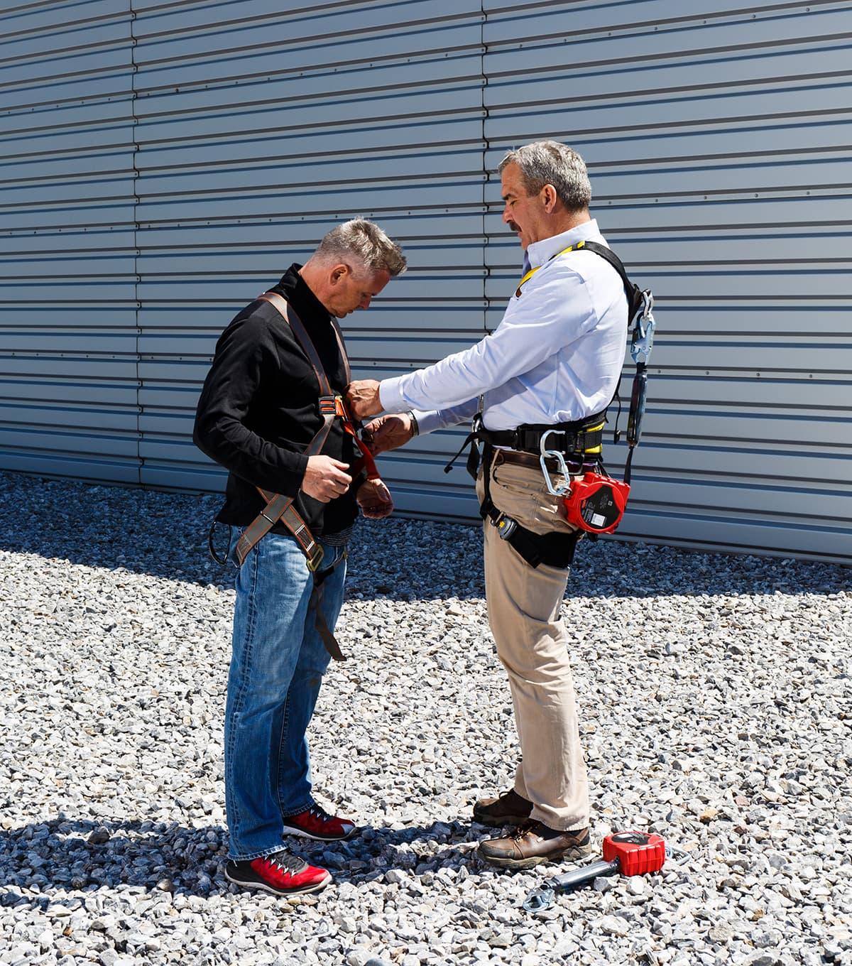 Two men wearing safety harness. One man is helping to adjust the other man's harness.